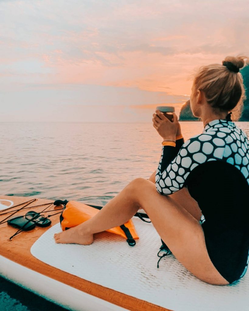 woman sitting on a sup board drinking tea out on the ocean. Wearing an ocean mimic black and white triggerfish design body suit 