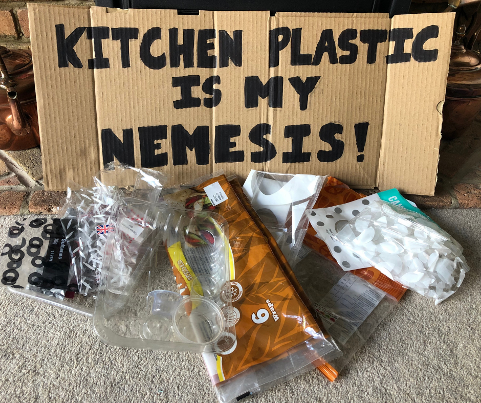 sign that reads 'kitchen plastic is my nemesis' with a pile of food wrappers in front of it
